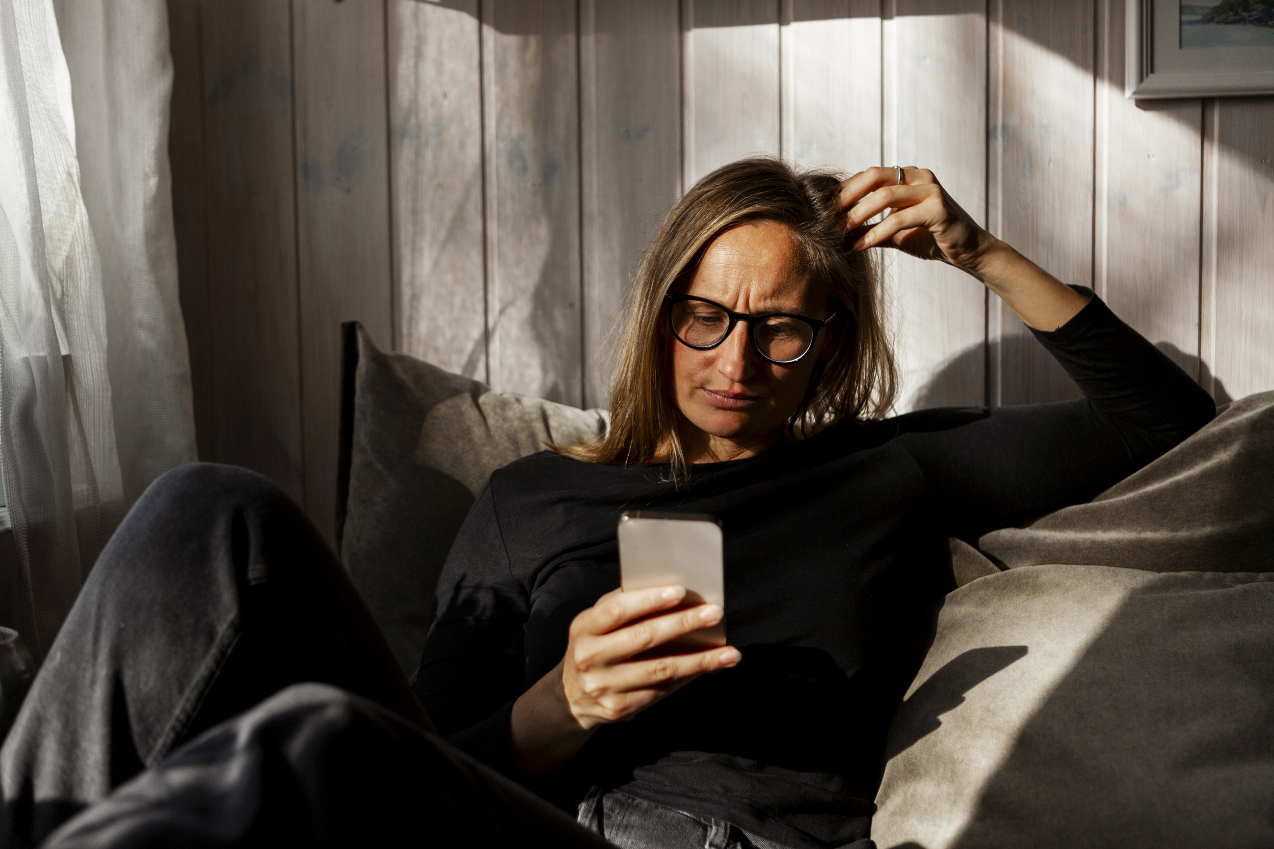 Kvinne som sitter innendørs i en sofa og ser ned på en mobiltelefon.
